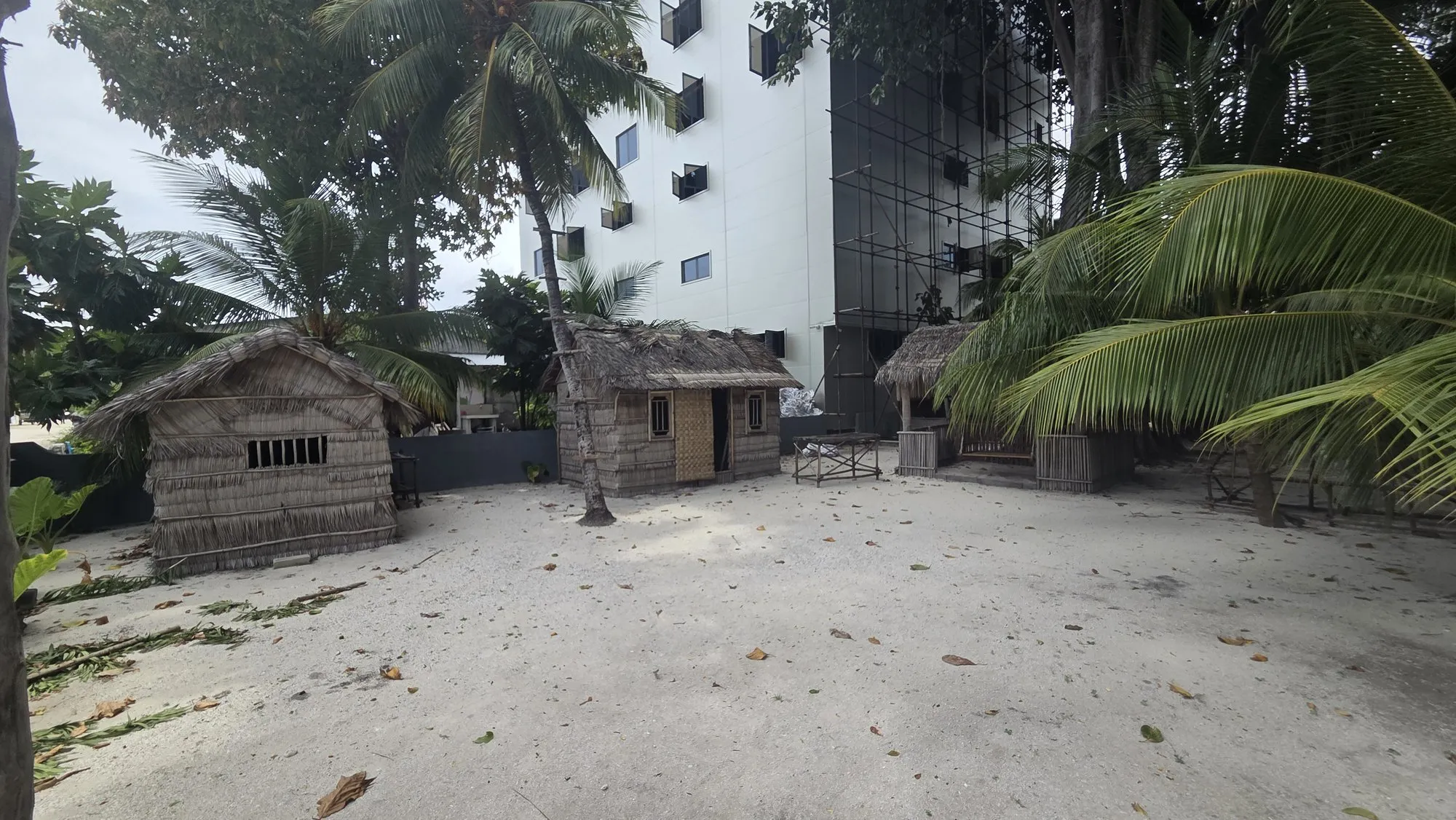 Traditionelle Palmhütten des Kulturdorfs von Kamadhoo, dahinter ein mehrstöckiger Hotelneubau mit Baugerüst.