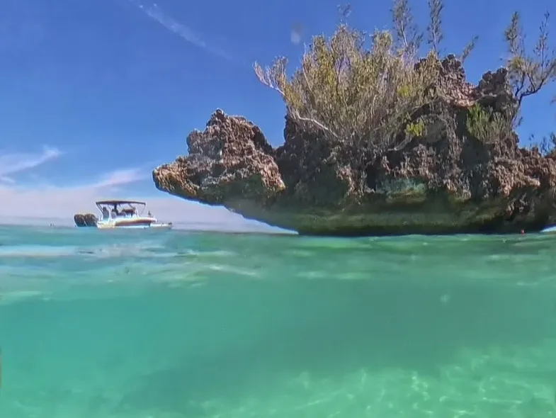 Halb über, halb unter Wasser: der Crystal Rock über der Lagune, darunter der helle Sandgrund, dahinter ein Boot.